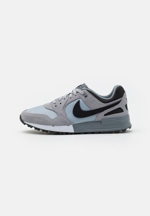 Harmaa ja musta Nike-tennari, jossa nauhat ja kuvioitu pohja, nähtynä sivulta valkoisella taustalla.