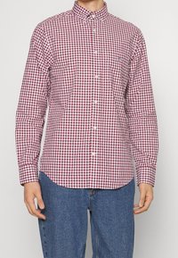 Rood-wit geblokte overhemden met kraag, een enkele borstzak en lange mouwen, gecombineerd met blauwe denim jeans.