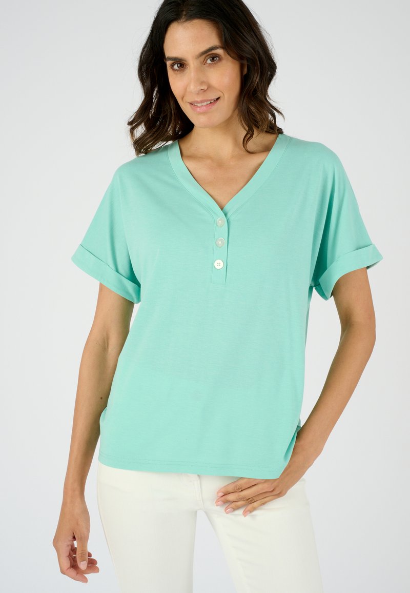 Camiseta de cuello en V color turquesa con mangas cortas enrolladas, que presenta tres botones decorativos en el escote. Tejido suave, corte relajado.