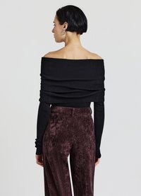 Schwarzer schulterfreier Pullover mit gerippter Struktur, kombiniert mit hoch taillierten, burgunderroten Samthosen mit sanftem Glanz.