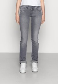 Jeans de mezclilla gris de corte ajustado, con bolsillos delanteros, cierre de botón y puños remangados. Combinados con zapatillas blancas.