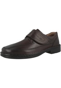 Brown leather shoe with a rounded toe, Velcro strap, and stitched detailing. Features a textured surface and low heel.