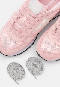 Rosa mocka- och nät-sneakers med texturerade accenter, med platta grå skosnören bredvid. Svart gummisula synlig.