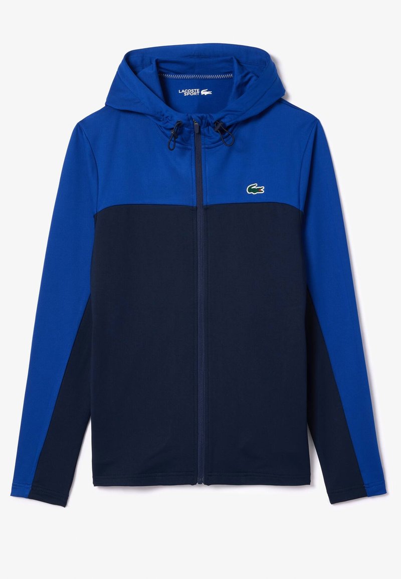 Blau- und marineblauer Kapuzenjacke mit Reißverschluss, langen Ärmeln, Kordelzug und kleinem grünen Lacoste-Krokodil-Logo auf der Brust.