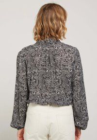 Blouse à motifs paisley noir et blanc avec des manches longues, un col haut et des détails froncés au dos ; tissu léger.