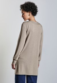 Långärmad beige topp i ett mjukt material, har en lös passform med sidsprund, i kombination med blå vida jeans.