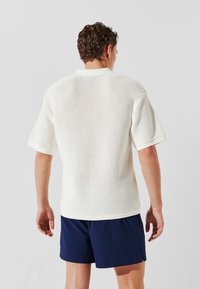 Un top alb tricotat cu mânecă scurtă, având un model texturat, cu croială dreaptă și guler ribborat, asortat cu pantaloni scurți bleumarin.