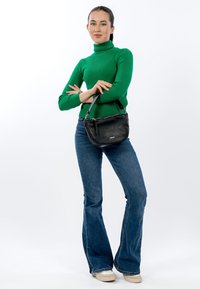 Czarna skórzana torebka na ramię o zaokrąglonym kształcie, z srebrnymi okuciami i pojedynczym paskiem, zestawiona z zielonym prążkowanym swetrem i rozkloszowanymi dżinsami.