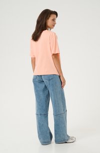Bawełniany t-shirt w kolorze brzoskwiniowym z krótkimi rękawami, zestawiony z jasnoniebieskimi dżinsami o szerokich nogawkach, z detalami szwów i luźnym krojem.