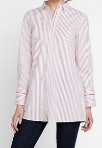 Chemise à manches longues boutonnée de couleur rose clair avec de fines rayures rouges, dotée d'un col et d'accents contrastants sur les poignets.