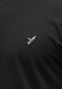 Μαύρο βαμβακερό μπλουζάκι με μικρό γκρι κεντητό σχέδιο πουλιού στο αριστερό μέρος του στήθους. Λεπτή υφή και άνετη εφαρμογή.