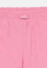 Shorts en coton rose avec un motif texturé, arborant des logos en relief et une taille élastique étiquetée "GUESS". Finition en tissu lisse.