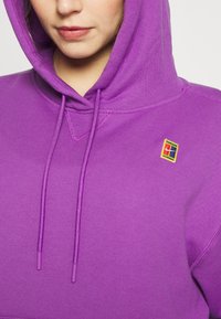 Felpa viola con cappuccio e lacci, decorata con un piccolo logo patch multicolore sul petto. Realizzata in un morbido tessuto testurizzato.