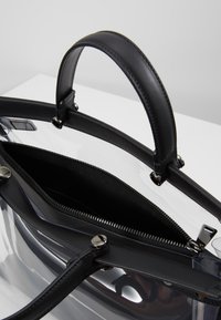 Borsa trasparente con manici e dettagli in pelle nera, dotata di una tasca interna con zip e dettagli in metallo.