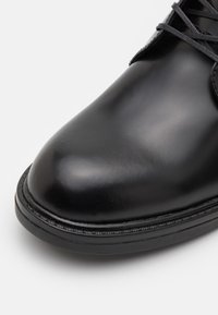 Pantof de piele neagră, cu vârful rotunjit și finisaj neted, având un design elegant și cusături subtile de-a lungul tălpii.