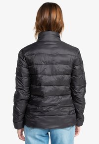 Svart puffjacka med hög krage, horisontellt quiltat mönster, glänsande yta och långa ärmar. Bärs över ljusblå jeans.