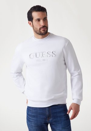 Felpa bianca con logo "GUESS" in rilievo, collo rotondo, polsini e orlo a costine. Abbinate a jeans blu in denim, texture liscia e design casual.