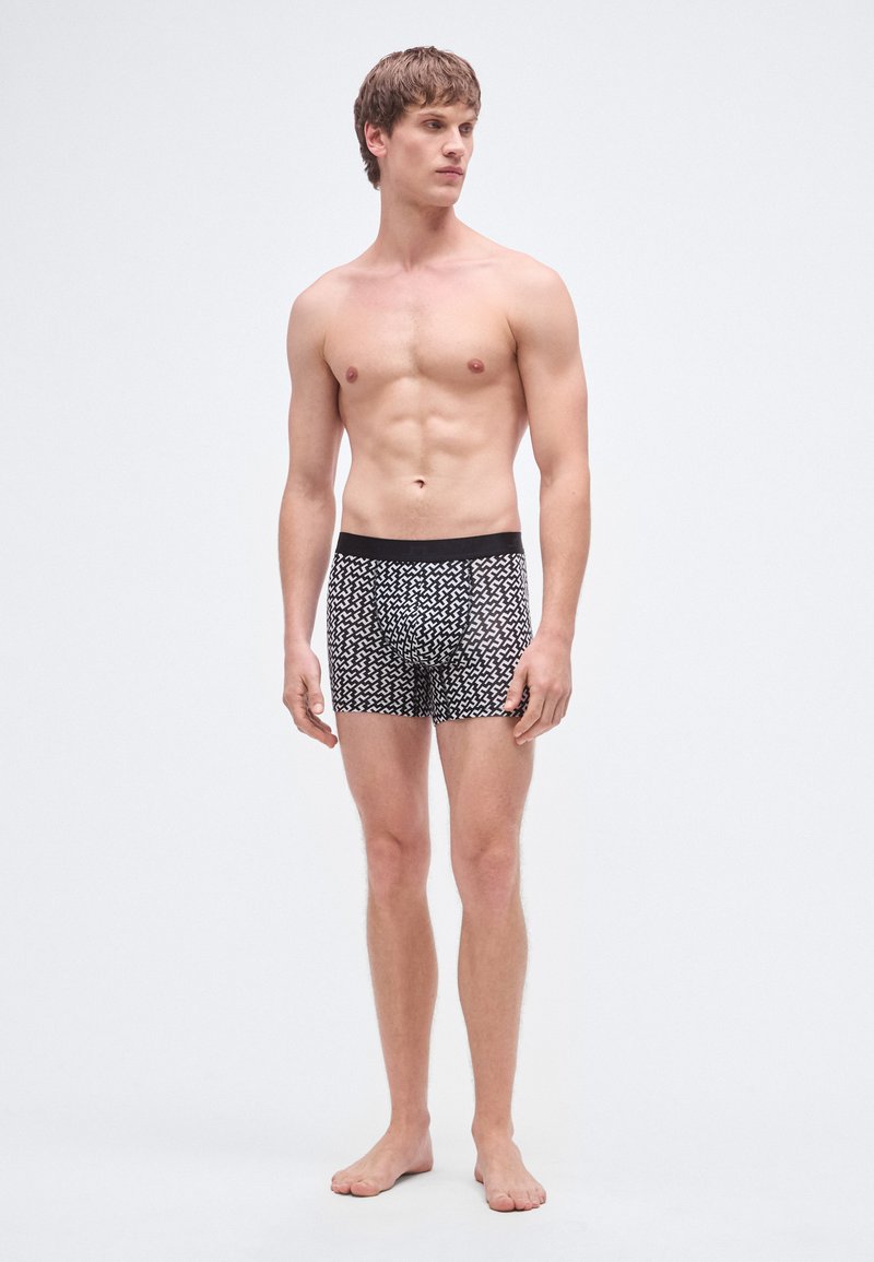 Cuecas boxer justas com padrão em preto e branco, com design ajustado e cintura elástica. O material parece macio com textura suave.