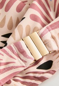 Tissu rose et beige avec des motifs abstraits, comportant un fermoir en ton doré. Matériau texturé et flexible avec un détail de couture le long des bords.