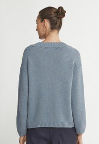 Jasnoniebieski sweter dzianinowy o luźnym kroju, z ribbowanym dekoltem i długimi rękawami. Teksturowana tkanina z lekko luźnym dołem w talii.