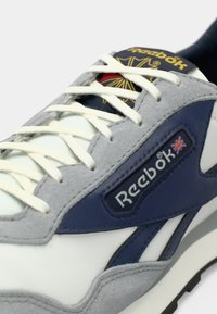Reebok tenisice s kombinacijom bijele kože, sive antilop kože i mornarskih naglasaka, s istaknutim logotipom i klasičnim vezanjem.
