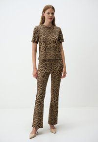Completo coordinato con stampa leopardata composto da un top a maniche corte e pantaloni a zampa in marrone e beige; tessuto morbido con una texture liscia.