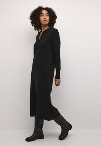 Black knit dress with long sleeves and a collar, featuring a front zipper. Paired with knee-high black boots and a smooth texture.