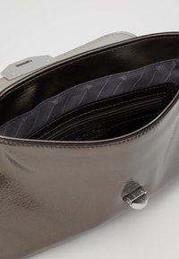 Grå patenteret læderhåndtaske med et slankt design, sølvhardware og et foret interiør med lynlåslommer og åbne lommer.