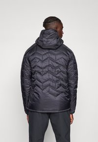 Schwarze gesteppte Pufferjacke mit Kapuze, die ein Zickzackmuster, eine glatte Textur und elastische Bündchen aufweist. Die Rückansicht zeigt das taillierte Design der Jacke.