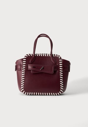 Sac à main en cuir bordeaux avec bordure blanche cousue, doubles poignées et rabat avant sécurisé par une fermeture à épingle argentée.