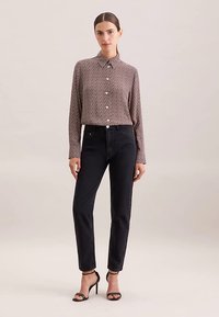 Braun gemustertes Hemd mit Knöpfen und Kragen, kombiniert mit hoch taillierten schwarzen Jeans und schwarzen Riemchensandalen. Glatter Stoff und maßgeschneiderte Passform.