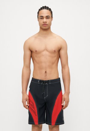 Shorts de bain noirs avec des panneaux latéraux rouges, taille avec cordon de serrage et coutures blanches contrastantes. Features logo sur le côté gauche.