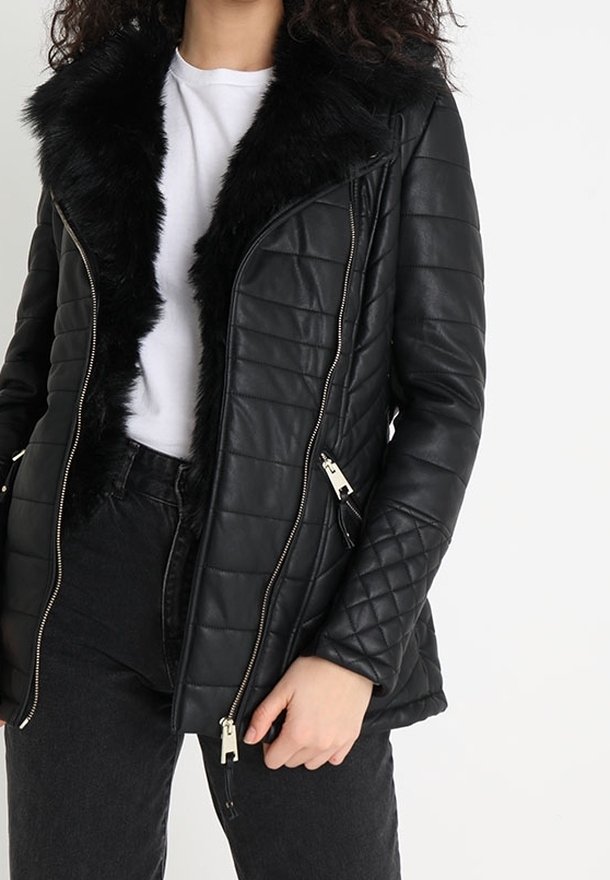 Chaqueta negra de cuero acolchada con cuello de piel sintética, con cremalleras plateadas y una forma ligeramente entallada. Se lleva sobre una camiseta blanca.