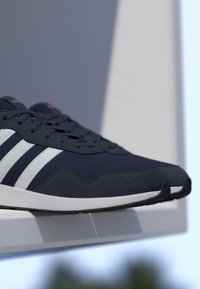 Zapatillas Adidas azul marino y blancas con tres rayas exhibidas en una estantería blanca contra un fondo exterior desenfocado.