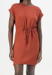 Šaty v rezavé barvě vyrobené z lehké tkaniny, s volným střihem, ohrnutými rukávy a nastavitelným páskem na šňůrku.