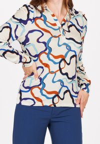 Pitkähihainen paita luonnonvalkoisesta kankaasta, jossa on abstrakteja pyörteitä sinisessä, oranssissa ja mustassa. Napillinen kaulus, muotonsa mukauttava ja gathered-hihansuilla.