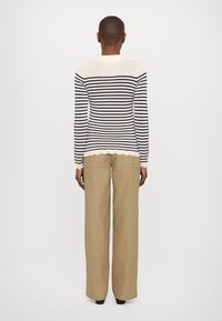 Námořnický a krémový pruhovaný pletený svetr se zaobleným lemem, v kombinaci s béžovými kalhotami s vysokým pasem, které mají dvě boční kapsy.