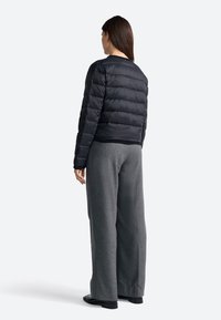 Giacca a vento nera con cuciture orizzontali, orlo a costine e collo rotondo. Indossata con pantaloni a gamba larga grigi. Sfondo uniforme.