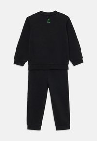Ensemble sweat-shirt et joggings noir Adidas, avec un logo vert dans le dos du haut et un design simple et moderne.