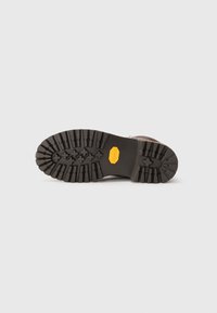 Sole of a brown boot with thick, rugged black tread and a yellow Vibram logo on a plain white background.