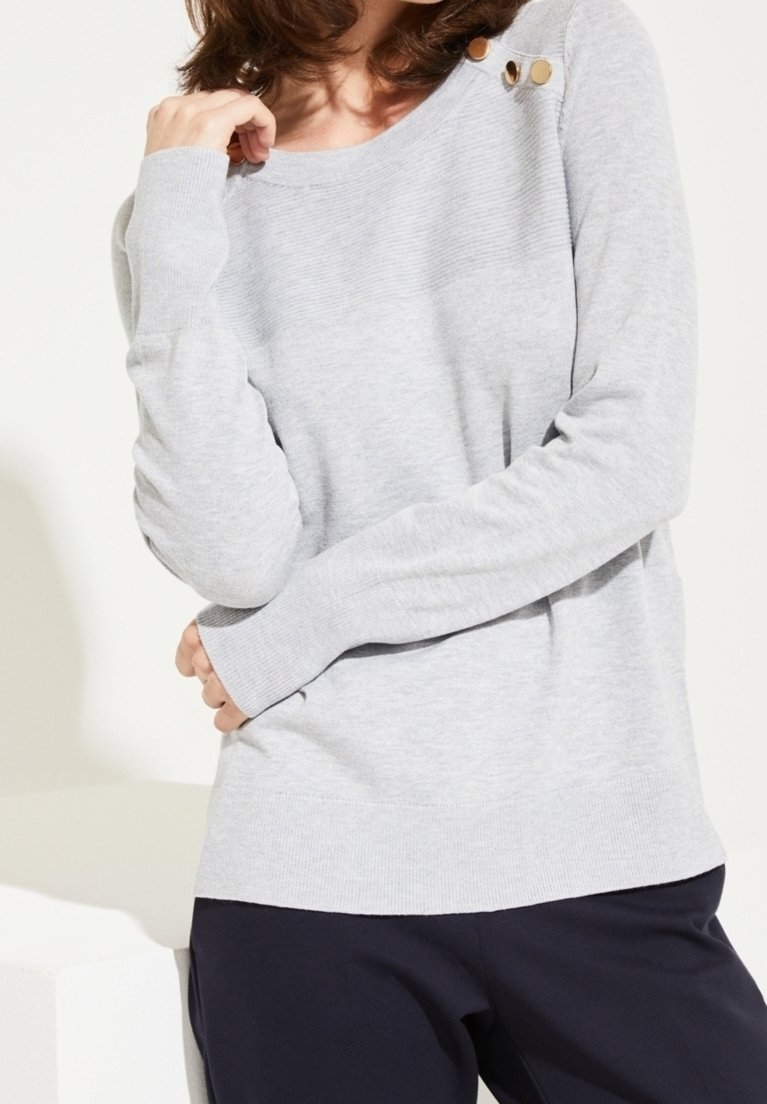 Suéter de punto gris claro con mangas largas, que presenta un escote redondo y tres botones decorativos en el hombro. Textura suave, corte casual.