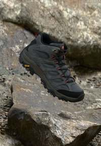 Black hiking shoe with a rugged design, mesh and synthetic upper, red accents, prominent lacing, and Vibram outsole for traction.