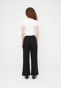 Λευκό τοπ με κοντά μανίκια συνδυα σμένο με μαύρο παντελόνι φαρδιάς γραμμής με υφασμάτινη υφή και ελαστική ζώνη μέσης. Μαύρα παπούτσια συμπληρώνουν το ντύσιμο.