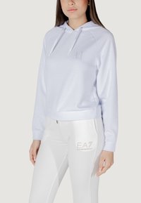 Felpa bianca con cappuccio regolabile e un piccolo logo grigio sul petto, abbinata a pantaloni bianchi con un'accattivante finitura in argento.