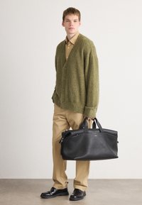 Groene getextureerde cardigan, beige shirt, khaki broek, zwarte leren tas met dubbele handgrepen en zwarte schoenen. Eenvoudige en functionele ontwerpelementen.