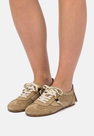 Chaussures à lacets en daim marron clair avec des détails perforés et des perles en bois décoratives, portées pieds nus sur un fond uni.