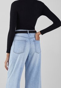 Haut noir à manches longues côtelé associé à un jean large bleu clair avec taille haute, poches arrière et ceinture noire cloutée.