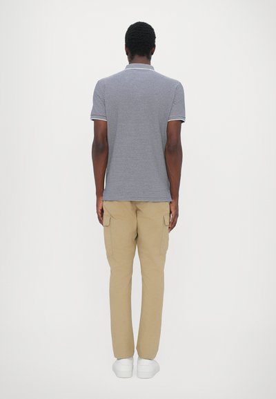 Camiseta de polo a rayas grises con mangas cortas, combinada con pantalones cargo beige y zapatillas blancas, vista desde la parte de atrás.