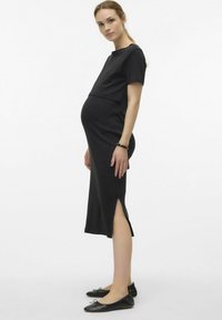 Robe de maternité noire à manches courtes et fentes latérales, en tissu doux. Portée avec des ballerines noires. Design simple et ajusté.