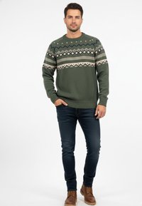 Suéter tejido verde con franjas horizontales estampadas en crema y azul marino. Cuello redondo, mangas largas, puños y dobladillo acanalados. Combinado con jeans oscuros y botas.